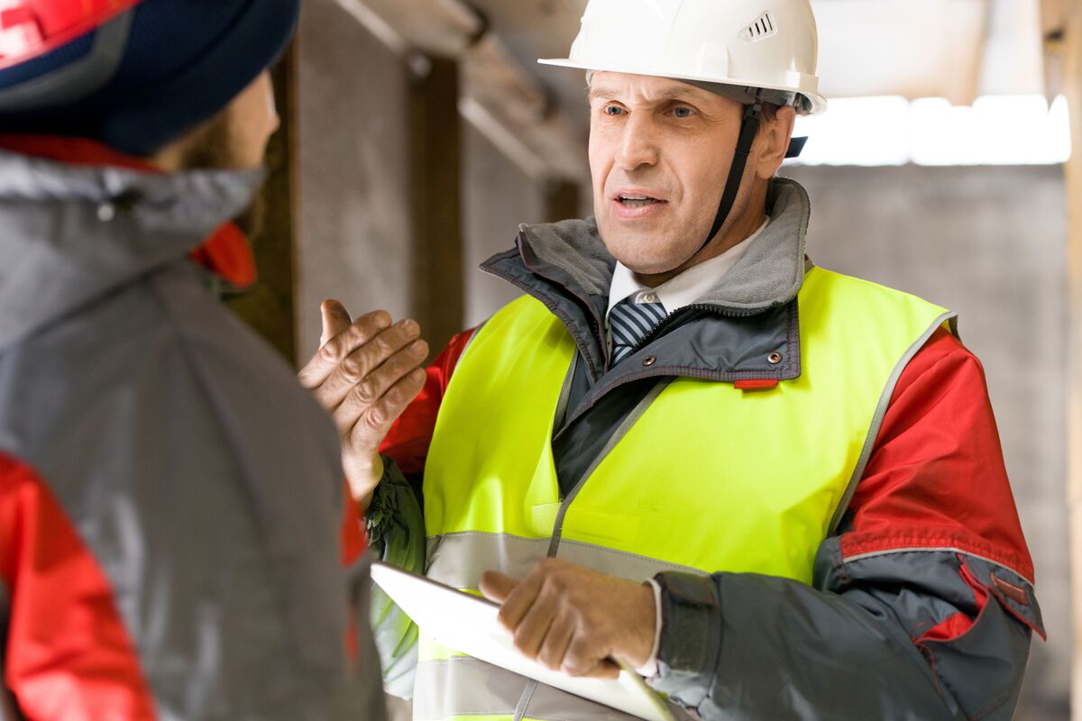 Construction supervisor wearing a hard hat and safety vest reviewing project details with a crew member on a job site.